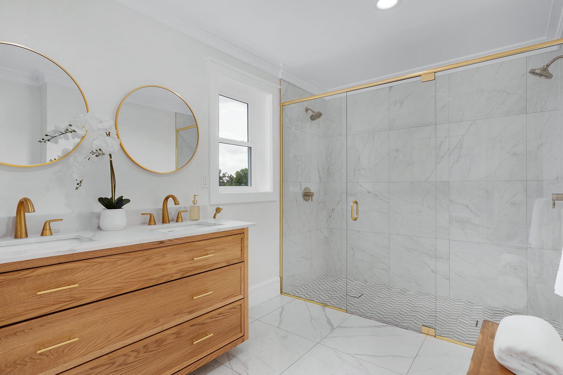 Primary bathroom with a floating white oak vanity, brass fixtures, and marble-tiled shower