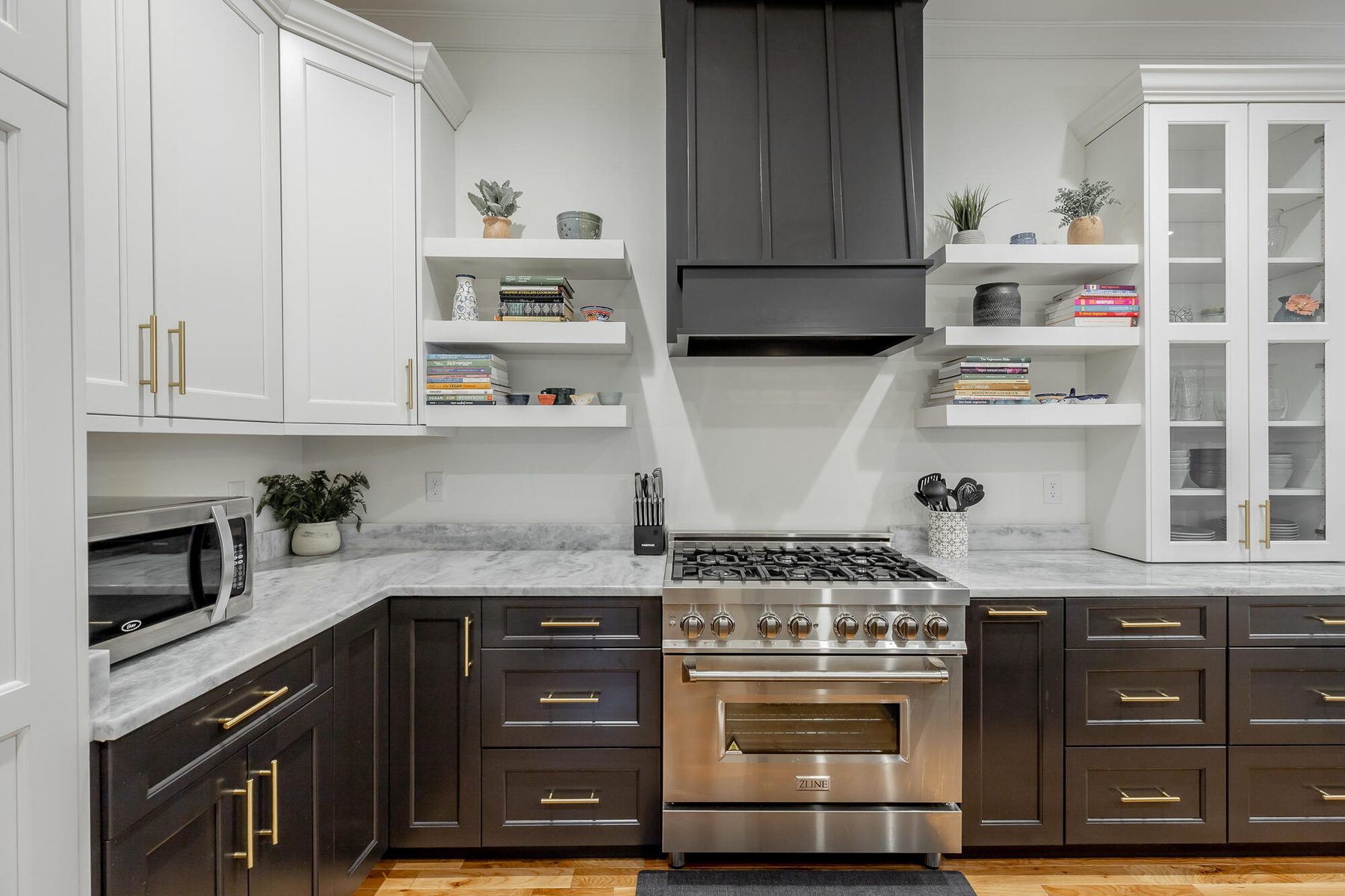 Two-tone kitchen in white and deep charcoal with a custom range hood, brushed brass hardware and glass-front upper cabinets in St. Elmo