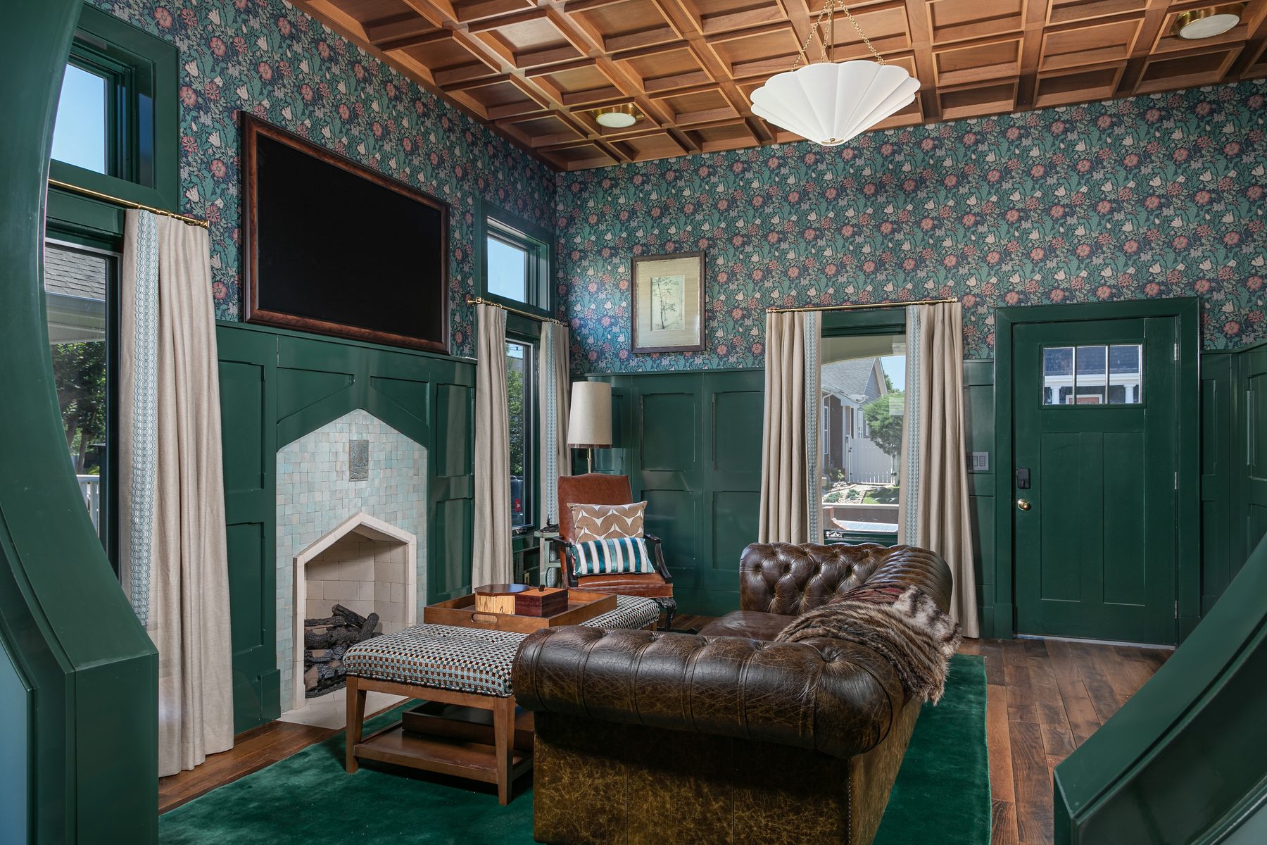 Living room in deep green panelling with a coffered mahogany ceiling and an arched stone fireplace at 1815 Williams Street